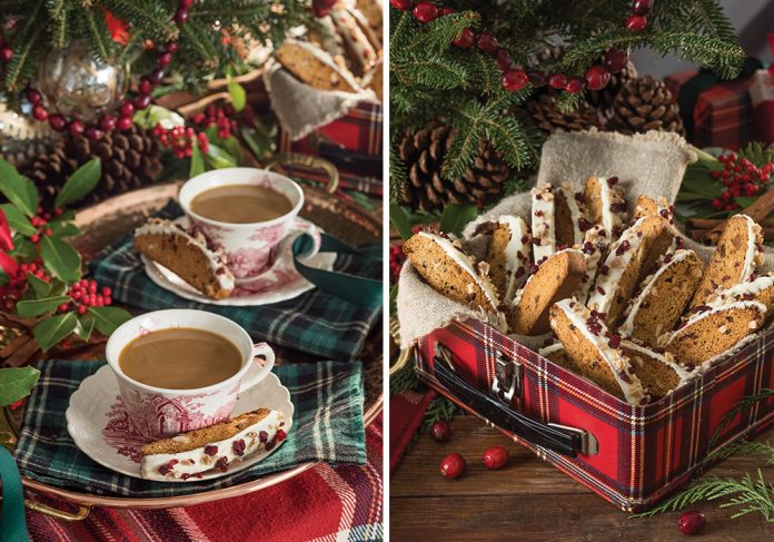 Our Gingerbread Biscotti spill from a red tartan lunch tin. Left: The same biscuits sit on the edge of a red-and-white teacup and saucer.