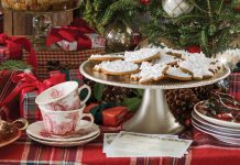 A buffet table set with various gingerbread recipes is dressed in red tartan linens and evergreen boughs.