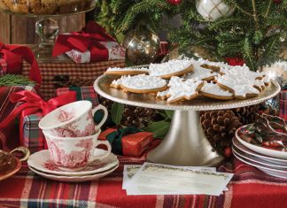 A buffet table set with various gingerbread recipes is dressed in red tartan linens and evergreen boughs.