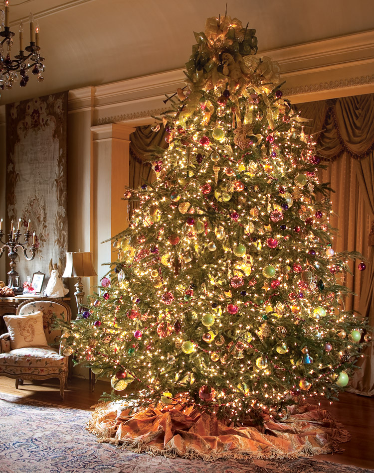 An image of grandeur in an open bedroom adorned with antiques, rugs, and tapestries, this tree is dotted with hundreds of glowing orbs in shades of gold, cherry red, and Granny Smith green.