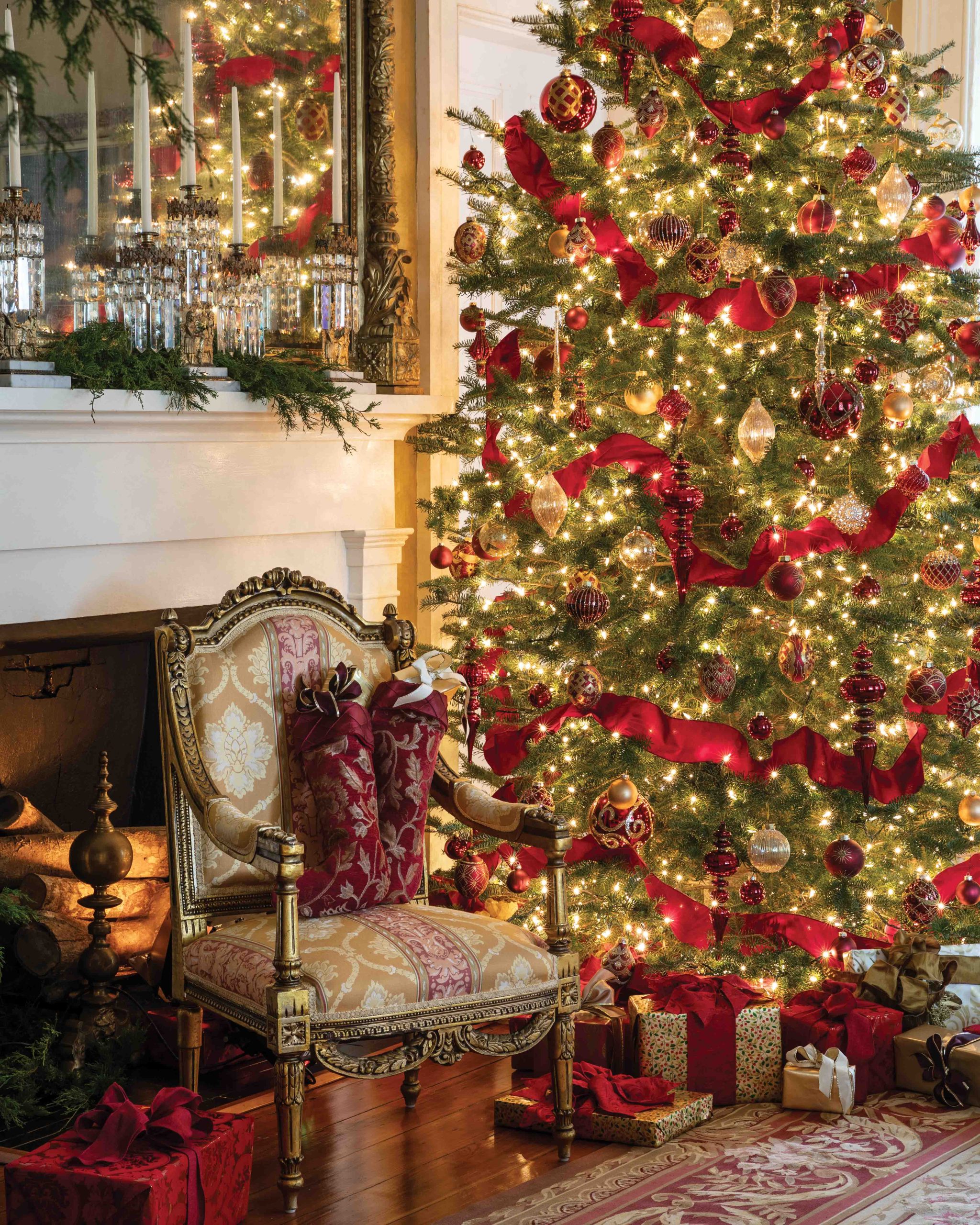 Red ribbons wrap around a regal Christmas tree dotted with gold and crimson hand-blown ornaments. The tree stands proud beside an antique French chair set before the hearth.