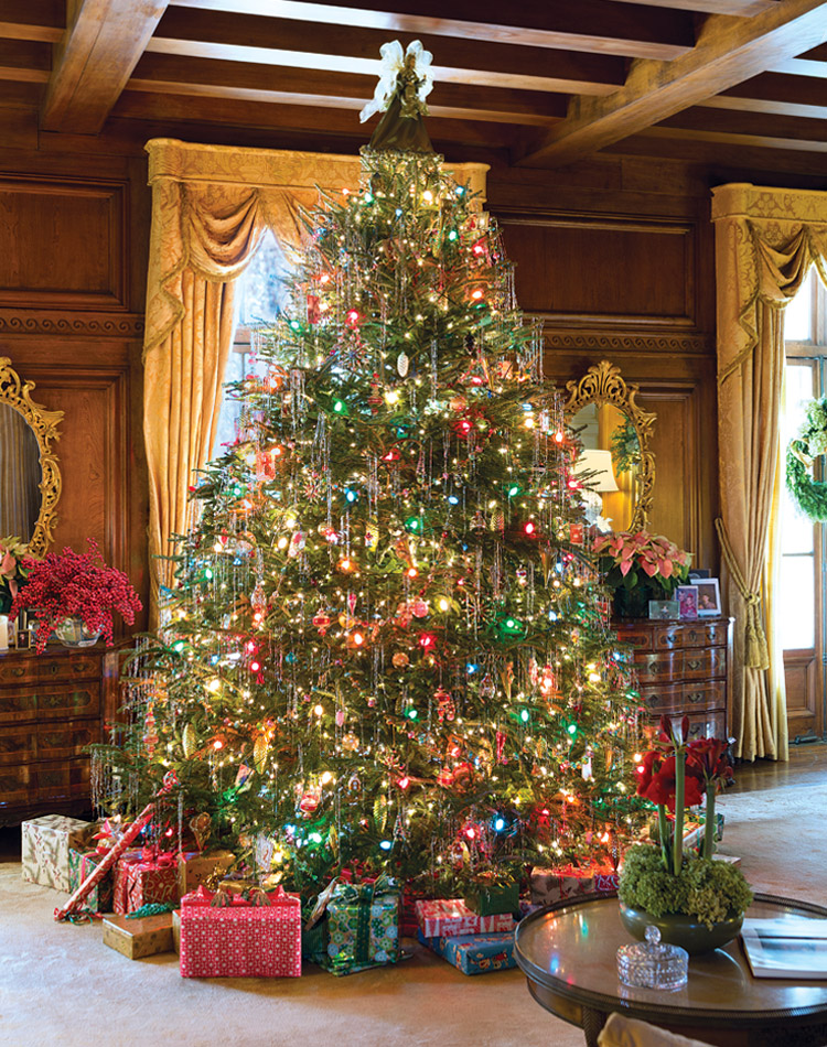 A Fraser fir Christmas tree is adorned with silver tinsel in a large room with wooden paneling and ornate gold curtains.