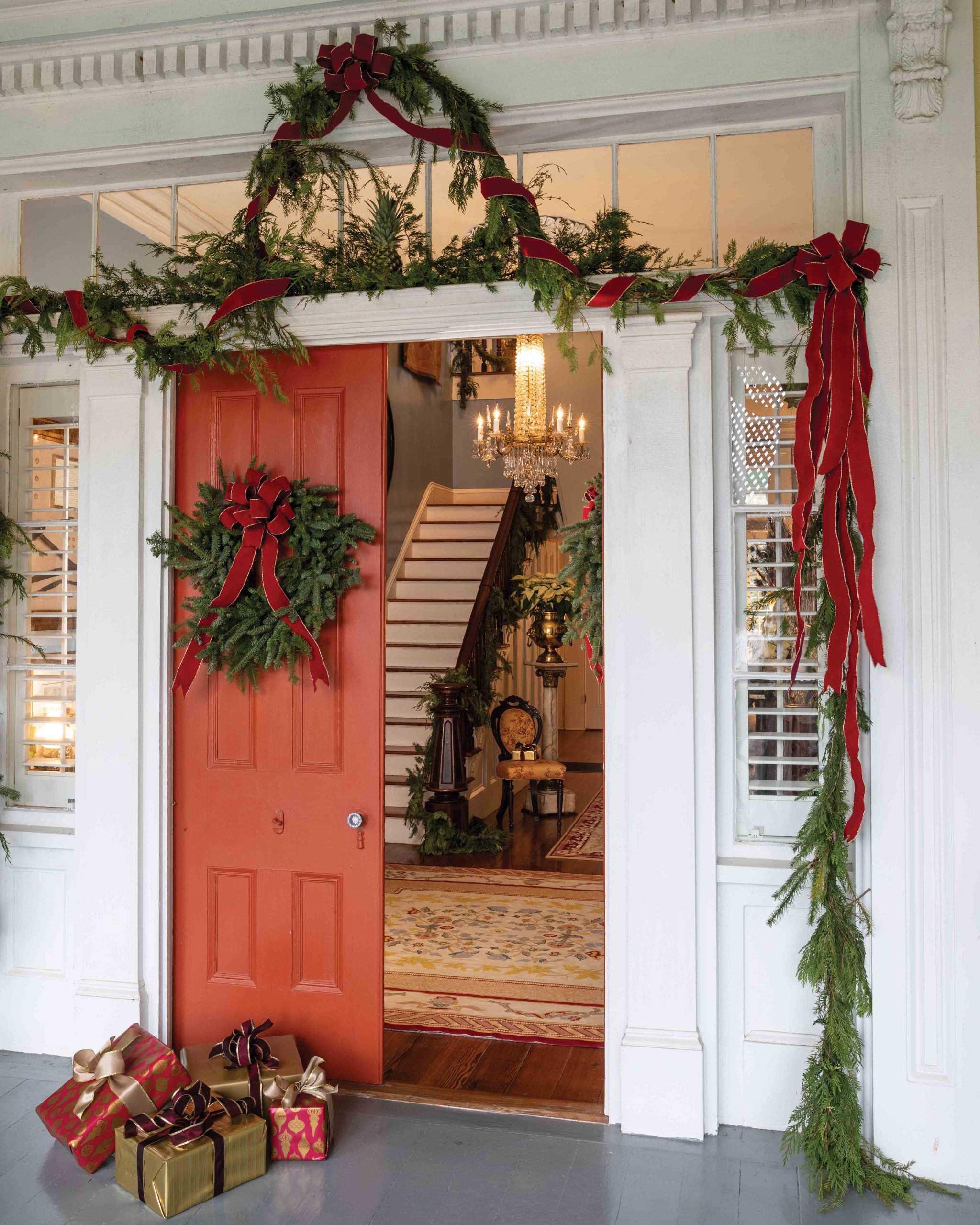 Simple evergreen garland wrapped with red ribbon coordinate with a traditional wreath upon the vibrant front door, welcoming the holiday season inside.