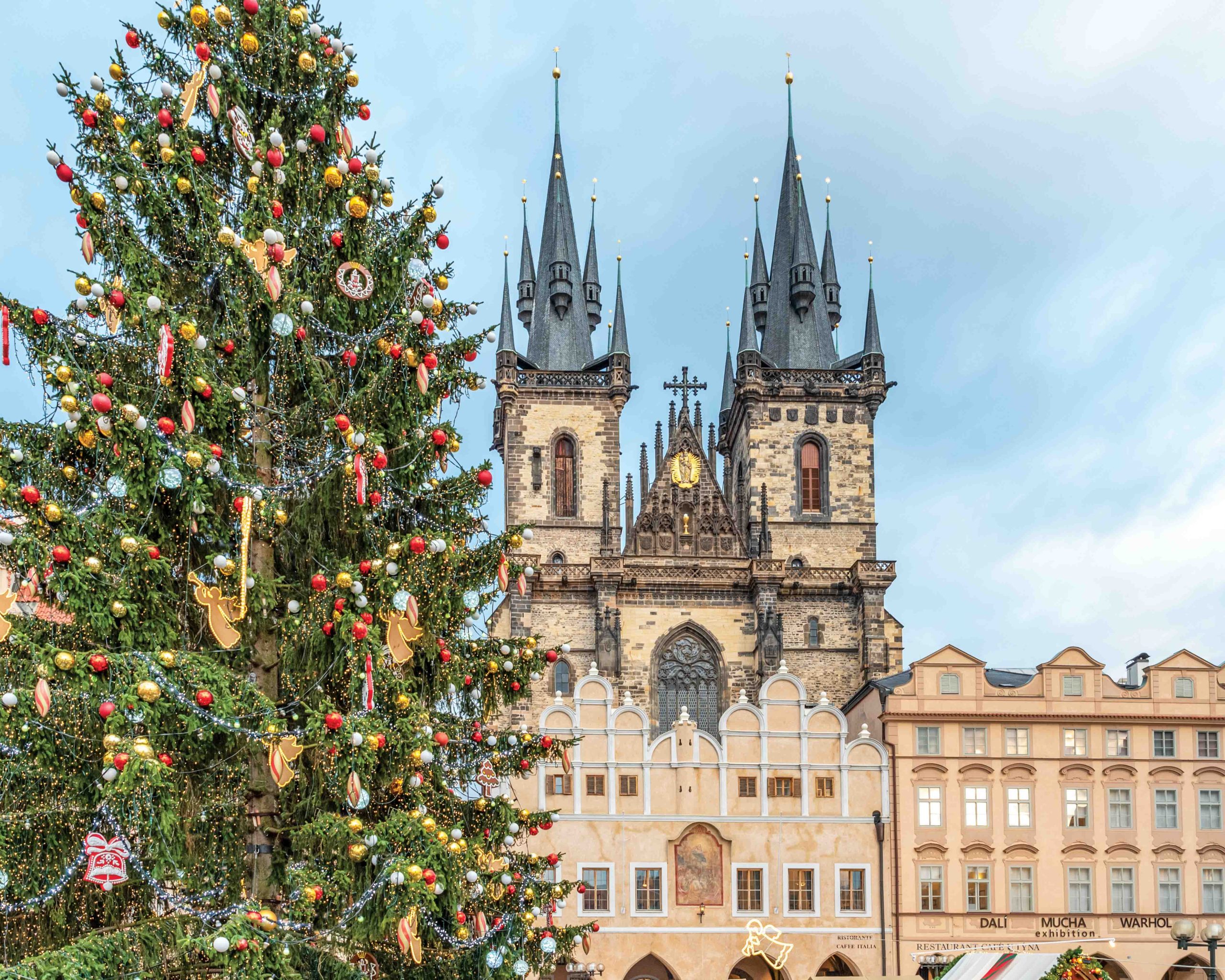 In Prague, the towering spires of the Church of Our Lady before Tyn rise above the square, with a decorated evergreen in the foreground.