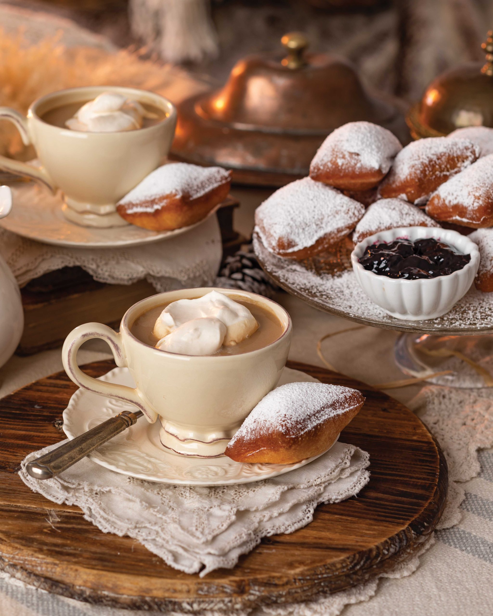 Confectioners’ sugar-sprinkled beignets and cozy white mugs of café au lait await indulgence atop a rustic table.