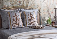 A breathtaking French bed is set against French Market Collection wallpaper and dressed in the brand’s antique motif pillows.