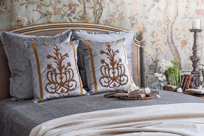 A breathtaking French bed is set against French Market Collection wallpaper and dressed in the brand’s antique motif pillows.