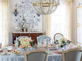 A rectangular dining table in Nicola Bathie McLaughlin’s Texas home displays a blue-and-white checked tablecloth, colorful china, and bouquets of pastel flowers.