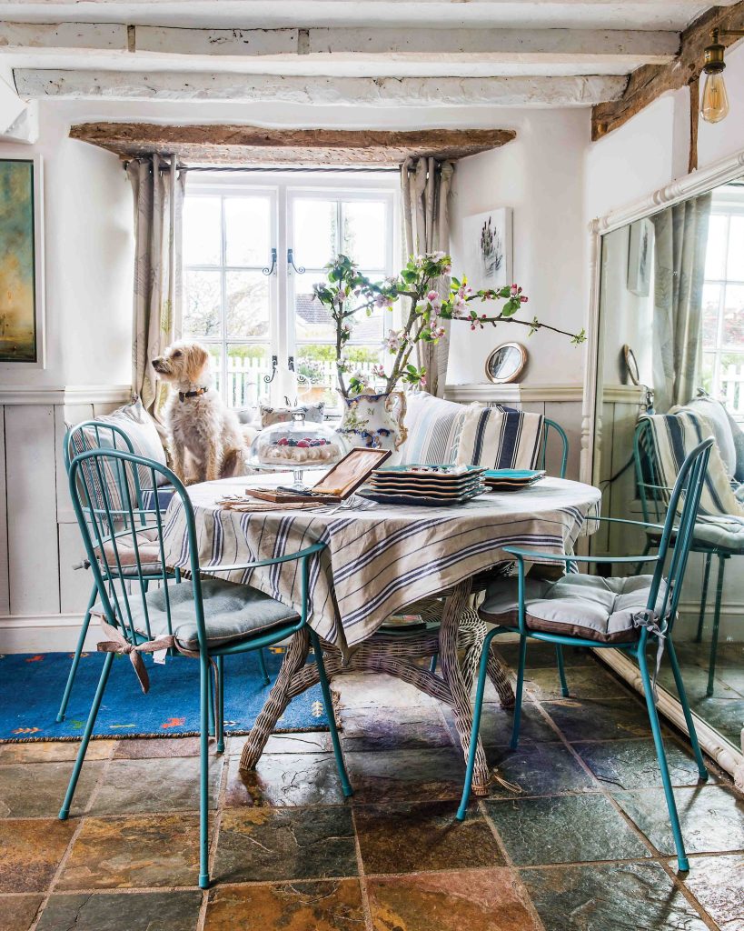 At the breakfast table, which is nestled beside a bright window, the homeowner’s sweet pup sits atop a blue chair.