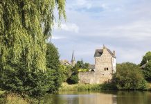 A calming view of the French countryside, with a village of stone buildings set beside a river bank and beneath a brilliant blue sky.